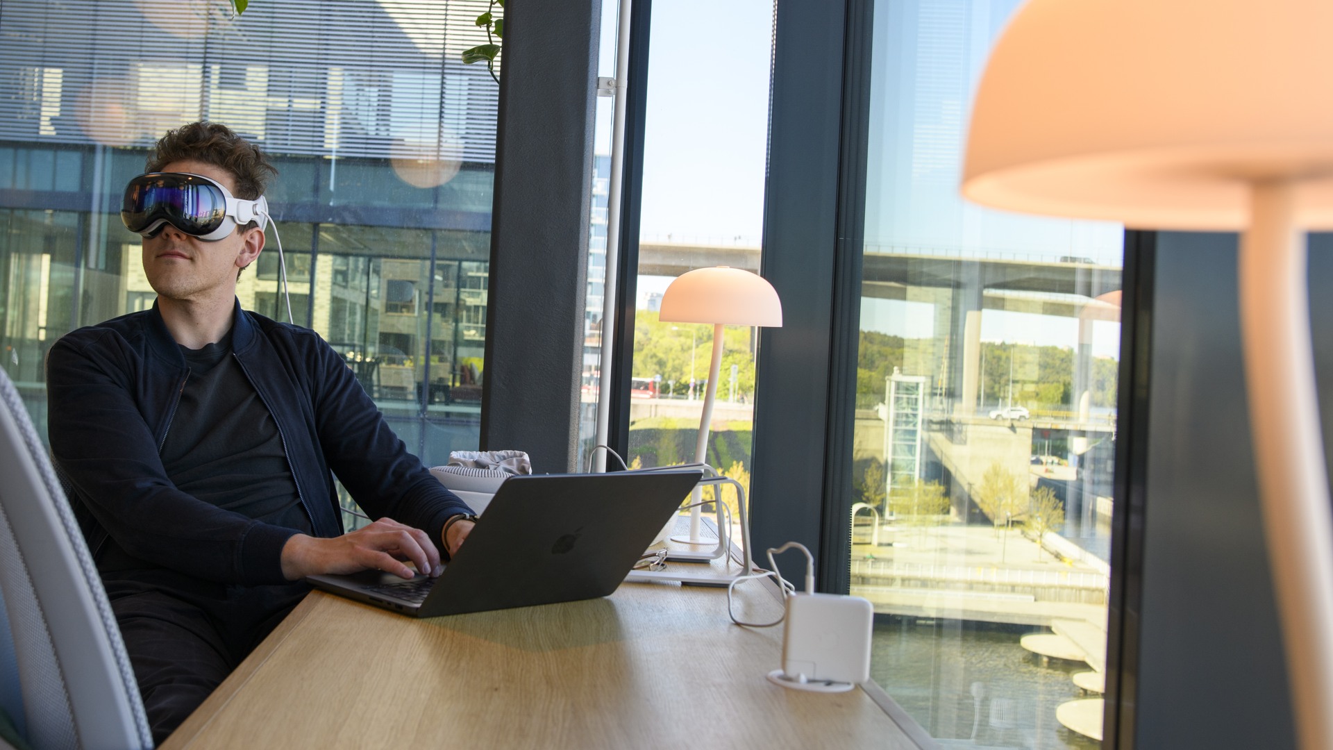 En man sitter vid ett skrivbord med en laptop på, han har VR-glasögon på sig.