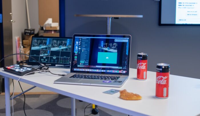 En laptop står på ett bord, bredvid står två cola-burkar.