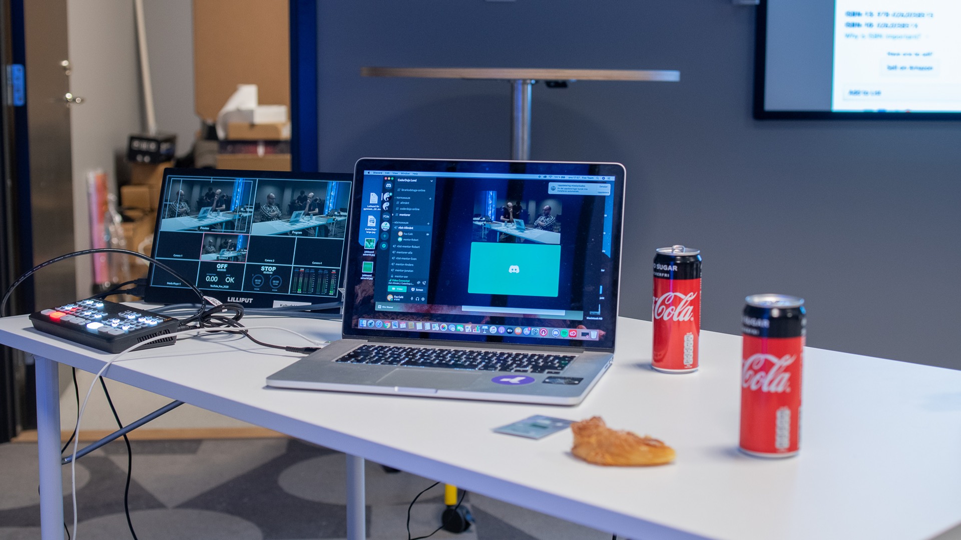En laptop står på ett bord, bredvid står två cola-burkar.