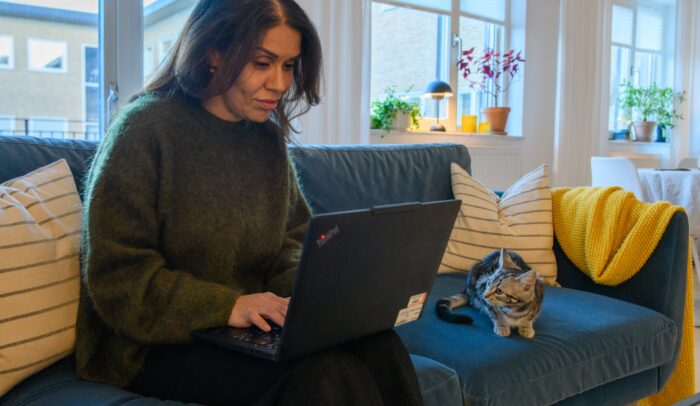 En kvinna sitter i en soffa och skickar e-post. Bredvid ligger en katt.