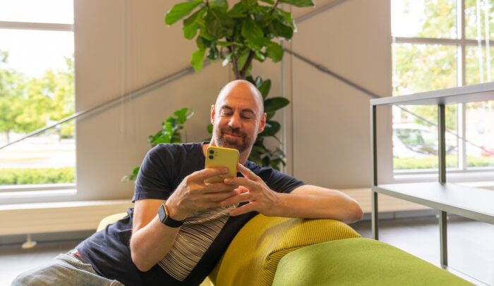 En man sitter i en soffa och scrollar på sin mobil.